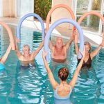 Senior group is doing aqua gym with swimming noodle in the swimm